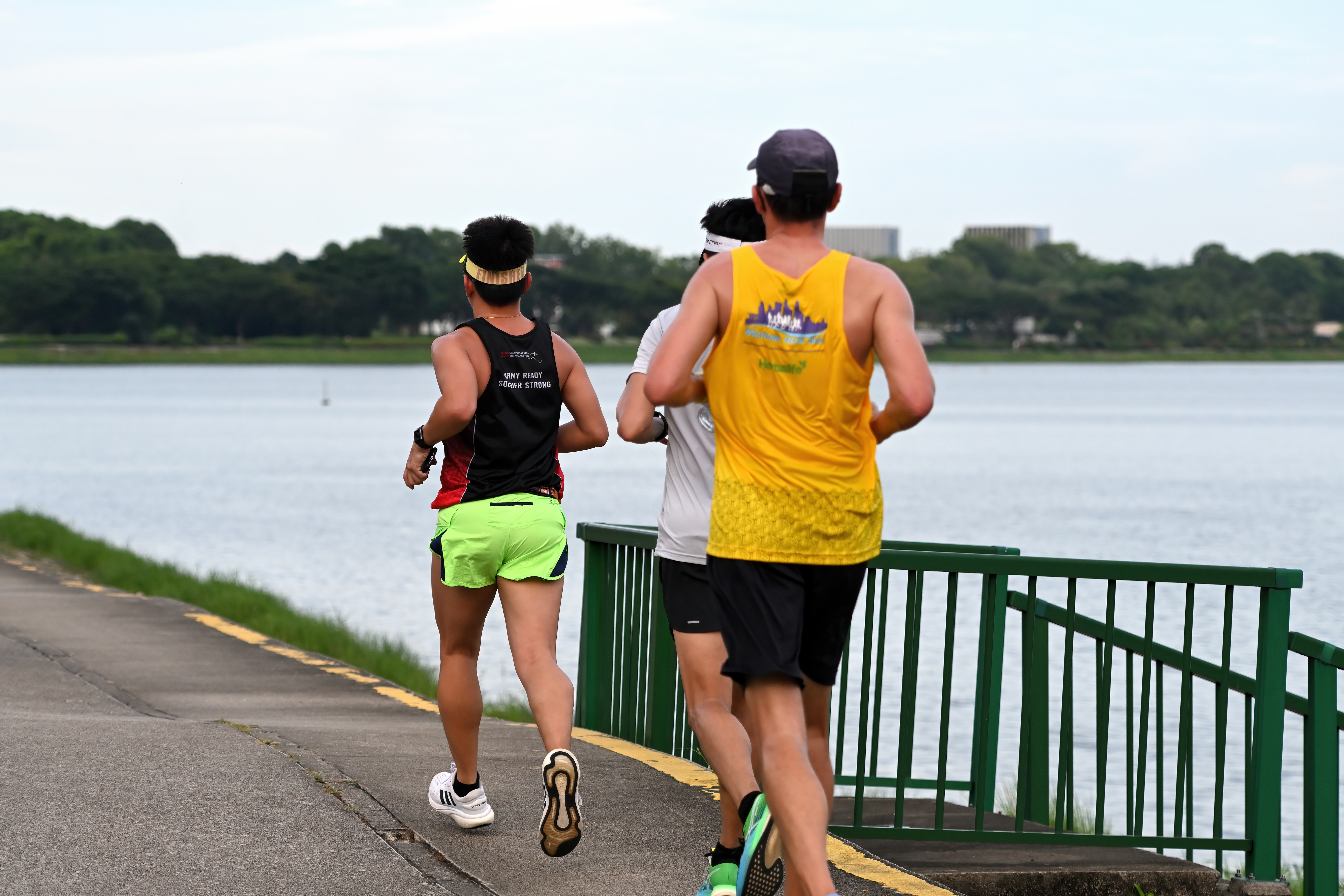 Three runners seen from behind, jogging along a path beside a reservoir.