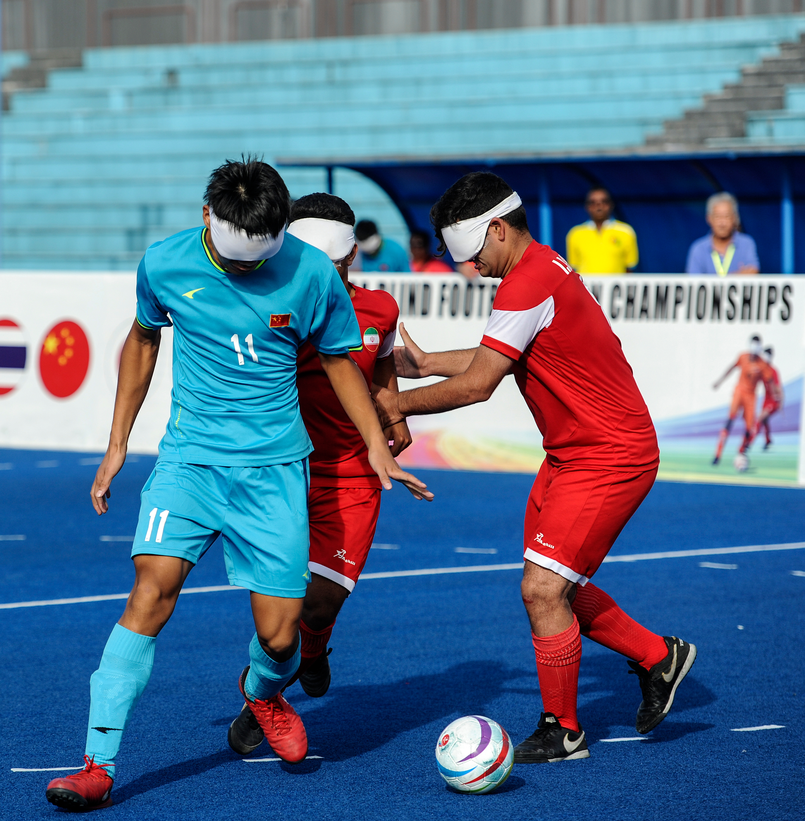 Blind football players wearing eye shades compete for the ball at a championship match.